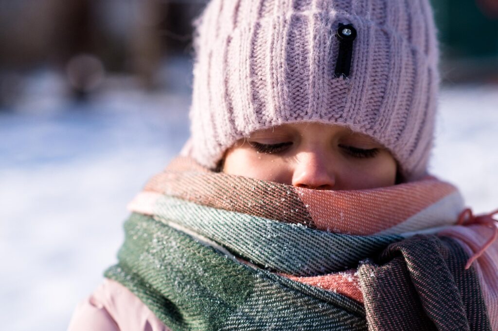 Rosto de criança agasalhada com touca e cachecol no frio, com neve, ilustrando urticária ao frio infantil